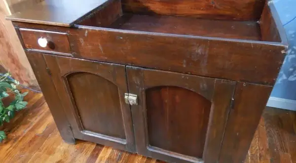 A vintage wooden dry sink with a drawer and cabinet doors, perfect for a rustic kitchen or bathroom.