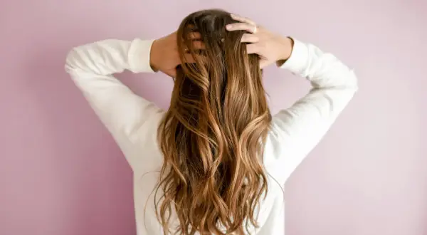 Mujer con pelos largos y ondulados, de color castaño, jugando con su cabello.