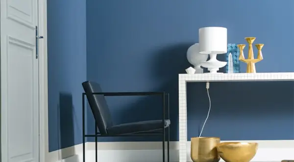Moderne Ecke mit schwarzem Sessel, weißer Tür und blau gestrichener Wand. Die Wirkung der Wandfarbe wird durch goldene Vasen und eine Lampe auf einem Tisch betont.