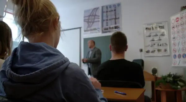 Uczniowie na kursie prawa jazdy, zastanawiają się, ile przed 18 można zdawać egzamin teoretyczny. Na ścianie znaki drogowe.