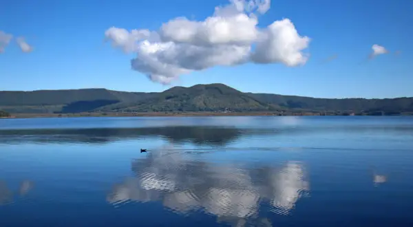 Un'oasi di pace al lago di Vici, con un cielo azzurro punteggiato da nuvole bianche che si specchiano sull'acqua calma.