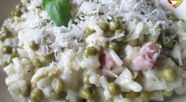 Creamy risotto with peas, ham, and grated cheese, garnished with a basil leaf.