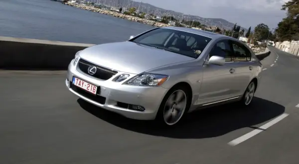Srebrny Lexus GS300 MK3 pędzi wzdłuż malowniczego wybrzeża z widokiem na zatokę pełną jachtów.