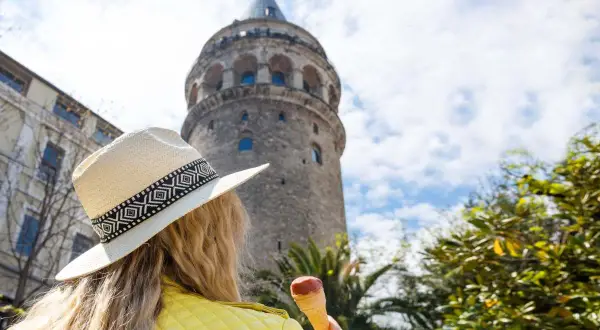 Kobieta w kapeluszu i żółtej kurtce je lody pod wieżą Galata w Stambule, Turcja.