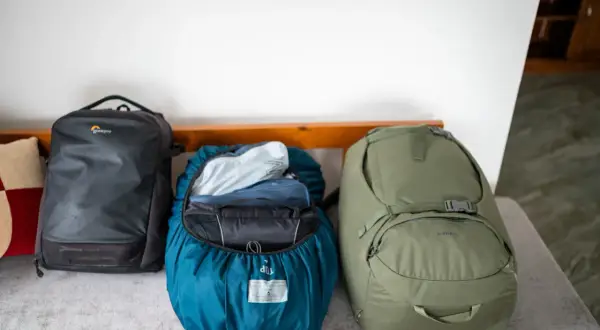 Drei Rucksäcke bereit für das Abenteuer. Ein schwarzer Lowepro, ein blauer mit Regenhülle und ein grüner Porter 65 – perfekt für das Asien Backpacking.
