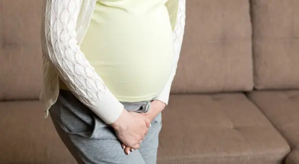 Kobieta w ciąży, z dłońmi przytrzymującymi brzuch, martwi się zielonym śluzem.
