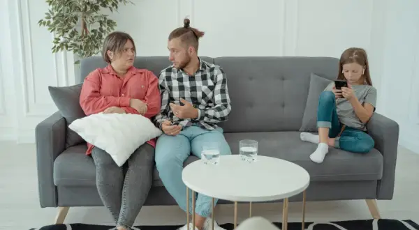 Rodzice rozmawiają z psychologiem rodzinnym, podczas gdy ich córka zajmuje się telefonem.