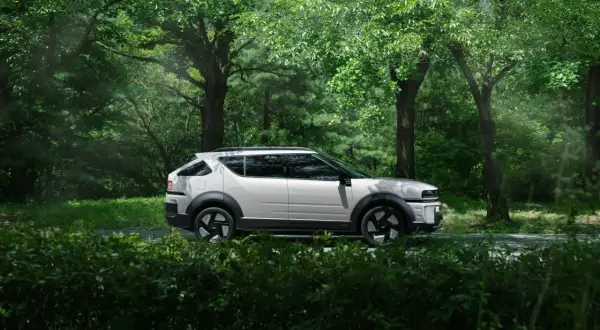 Biały Tucson Hybrid na tle zielonego lasu. Niskie spalanie to jego atut podczas podróży po malowniczych trasach.