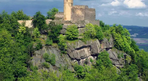 Zamek Chojnik góruje nad skalistym zboczem, otoczony bujną zielenią drzew.