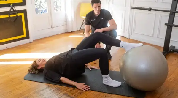 Un coach supervise une femme effectuant des exercices de rééducation avec une prothèse de hanche, évitant les mouvements interdits.