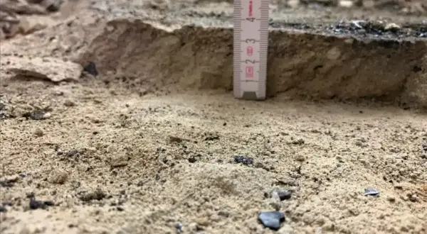 Mesure de la profondeur du décaissement du sol avec une règle. Le sable et les débris sont visibles.