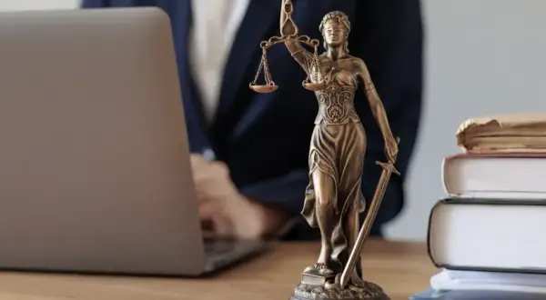 Justitia-Statue neben Laptop und Büchern. Ein Anwalt prüft Unterlagen, vielleicht wegen eines Widerspruchs Pflegegrad.