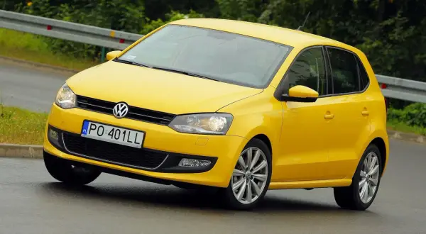 Żółty Volkswagen Polo 6R na mokrej drodze, z tablicą rejestracyjną PO 401LL.