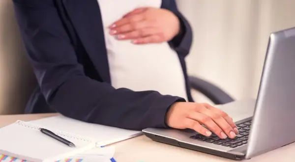 Kobieta w ciąży przygotowuje wniosek o urlop macierzyński, pracując przy laptopie.