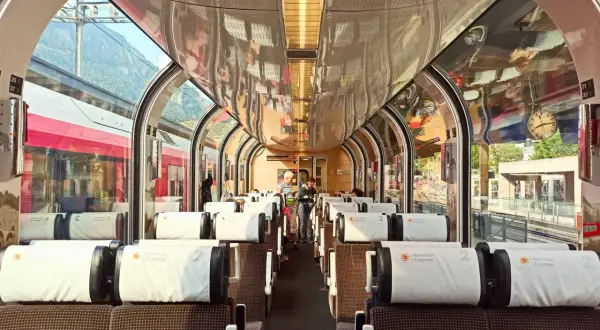Wnętrze pociągu panoramicznego Bernina Express z wygodnymi siedzeniami i dużymi oknami, przez które widać góry.