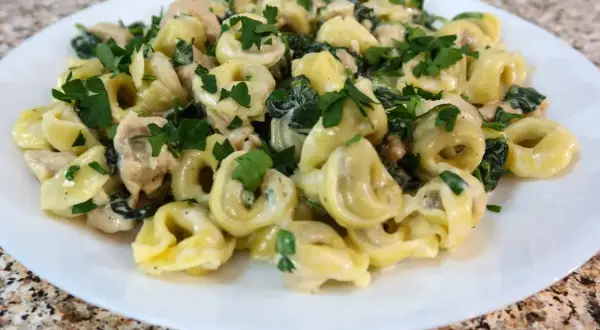 Tortellini z ricottą i szpinakiem w kremowym sosie, posypane natką pietruszki. Idealne danie, które można podawać samo lub z dodatkiem kurczaka.