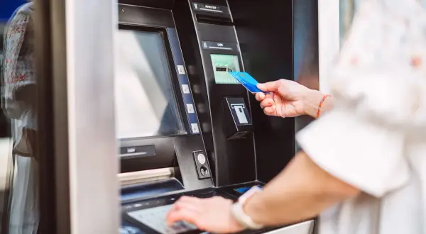 Kobieta wkłada kartę do bankomatu, przygotowując się, jak wziąć debet. Wpisuje PIN na klawiaturze.