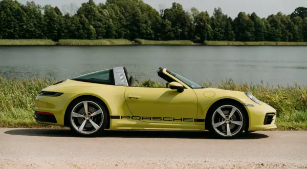 Żółty Porsche Targa z czarnym napisem na progu, zaparkowany nad jeziorem, otoczony zielenią.