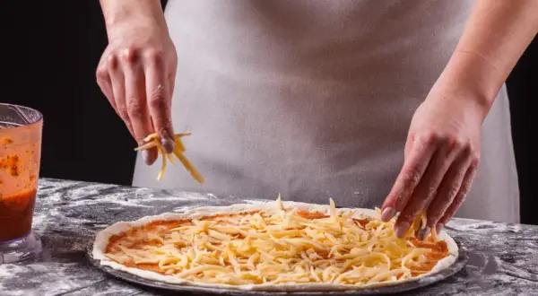 Ręce posypują pizzę startym serem. Zastanawiasz się, jaki ser do pizzy będzie najlepszy? Ten wygląda apetycznie!