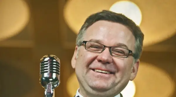 Artur nagrał płytę myśliwiecka. Uśmiechnięty mężczyzna w okularach stoi przy mikrofonie.
