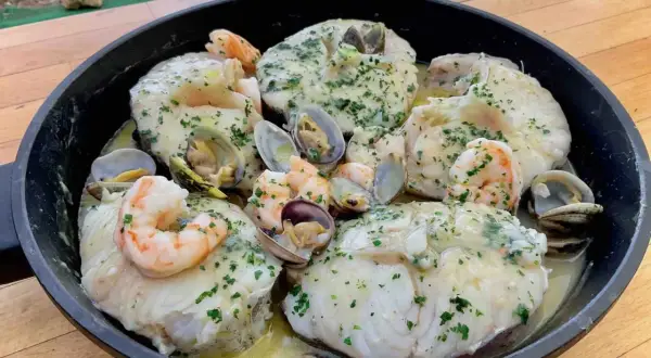 Merluza con almejas y gambas en una sartén, con perejil picado y salsa cremosa. ¡Un plato marinero delicioso!