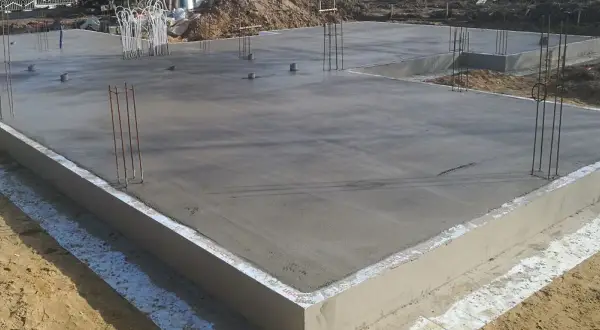 Świeżo wylany betonowy fundament pod dom, z wystającymi prętami zbrojeniowymi. To kluczowy etap, jak zrobić fundament pod dom, zapewniający stabilność konstrukcji.