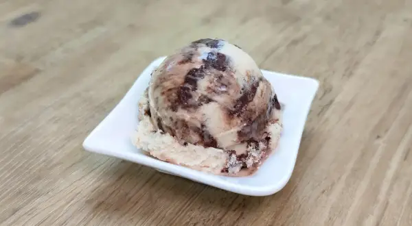 Ein Löffel cremiges Kinderriegel Eis mit Schokoladenstückchen auf einer weißen Schale.
