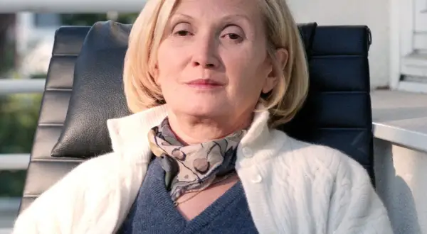 Barbara Sołtysik w białym swetrze i apaszce, siedzi w czarnym fotelu. Jej twarz wyraża spokój, mimo że zmaga się z chorobą.