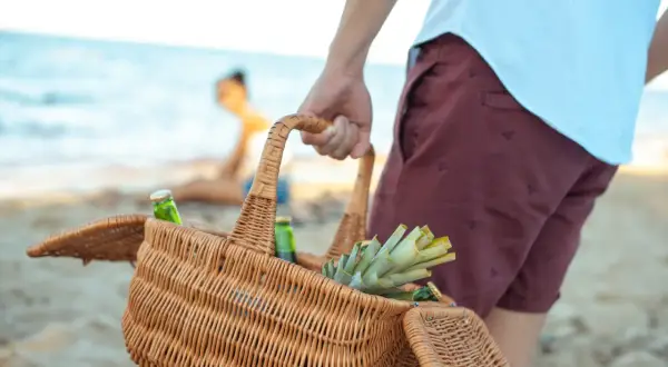 Koszyk z napojami i ananasem, idealne przekąski na plażę. W tle widać parę odpoczywającą nad morzem.