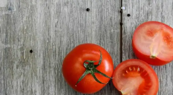 Tomates frescos, uno entero y dos cortados por la mitad, sobre una tabla de madera. Son un ejemplo de 10 alimentos umami.