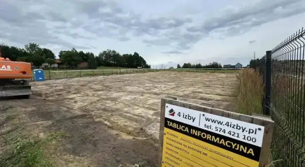 Tablica informacyjna budowy na placu budowy z koparką i toaletą.