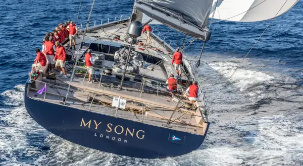Equipaggio in rosso sul My Song yacht, che solca le onde blu. La vela nera e bianca cattura il vento.