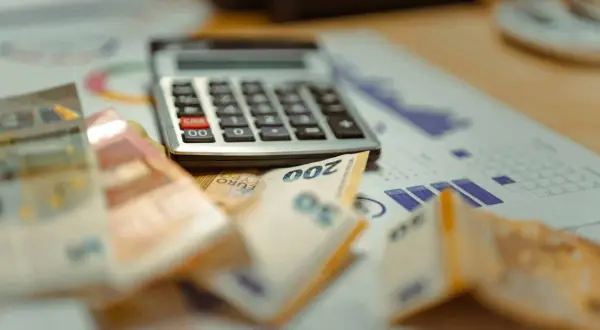 Kalkulator, banknoty euro i wykresy na biurku.