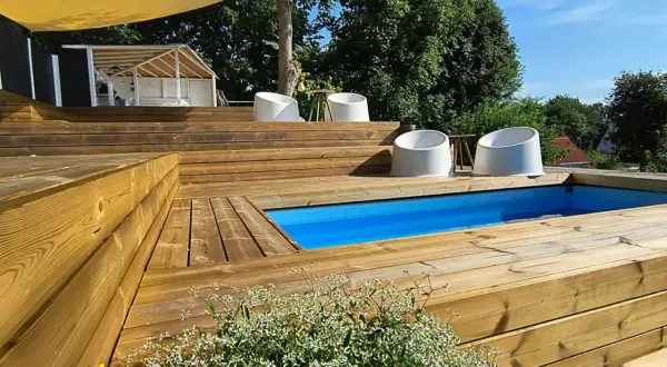 En härlig altan med nivåskillnad och pool. Vita stolar står utplacerade på de breda trätrappstegen.