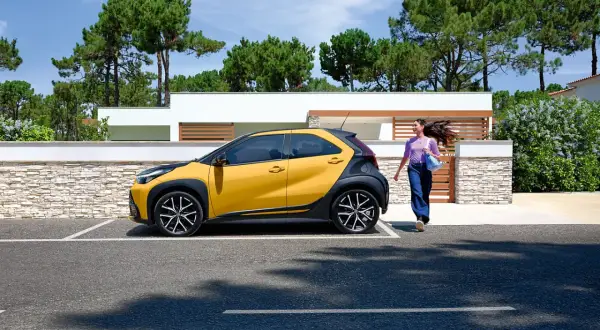 Une jeune femme se dirige vers sa voiture jaune et noire, une **voiture jeune permis automatique** parfaite pour débuter.