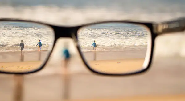 Okulary korygujące widok na plażę z dziećmi wchodzącymi do morza.