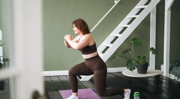 Frau macht einen Ausfallschritt auf einer Matte, ein effektiver bauch workout. Sie trägt braune Sportkleidung und weiße Socken.