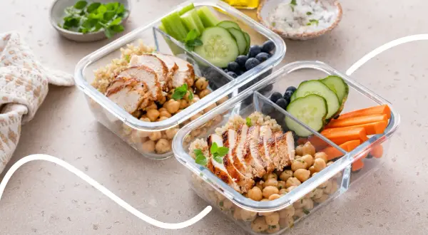 Zwei Behälter für Meal Prep mit Hähnchenbrust, Kichererbsen, Quinoa, Gurke, Karotten und Blaubeeren.