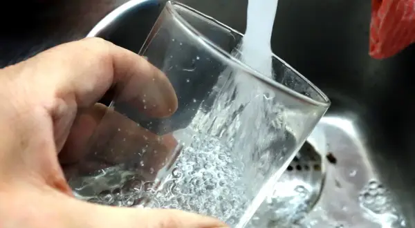 En hand håller ett glas som fylls med vatten från en kran. Ja, kan man drikke vann fra springen i Sverige, det är rent och gott!