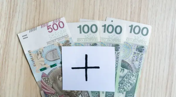 Polskie banknoty 500 i 100 zł. Na białej kartce symbol plusa, sugerujący dodatkowe środki, np. specjalny zasiłek opiekuńczy.