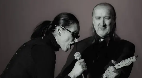 Kora śpiewa do mikrofonu, a obok niej gra na gitarze muzyk. To scena z koncertu, gdzie można usłyszeć maanam piosenki alfabetycznie.