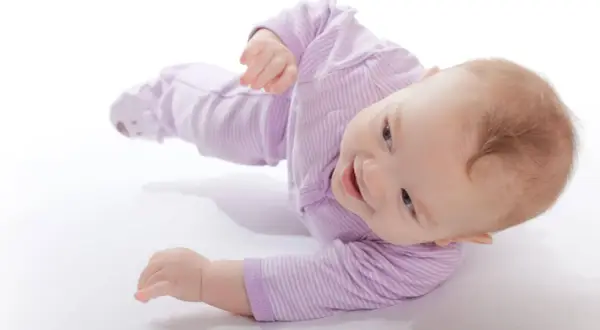 Uśmiechnięty niemowlak w fioletowym pajacyku uczy się obracać. To świetna zabawa i ważny etap rozwoju.