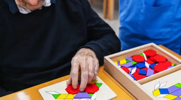Un senior concentré assemble un puzzle coloré, un jeu mémoire senior stimulant.
