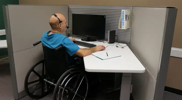 Mężczyzna na wózku inwalidzkim pracuje przy biurku, co pokazuje, że **ableizm** nie powinien ograniczać możliwości zawodowych.