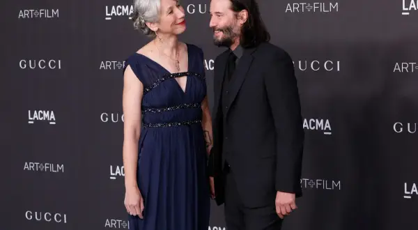 Keanu Reeves i jego żona Alexandra Grant patrzą na siebie z uśmiechem na tle logo Gucci i Art+Film.