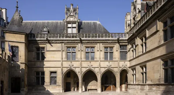 Hof des Musée de Cluny mit gotischer Architektur, Spitzbögen und filigranen Verzierungen unter blauem Himmel.