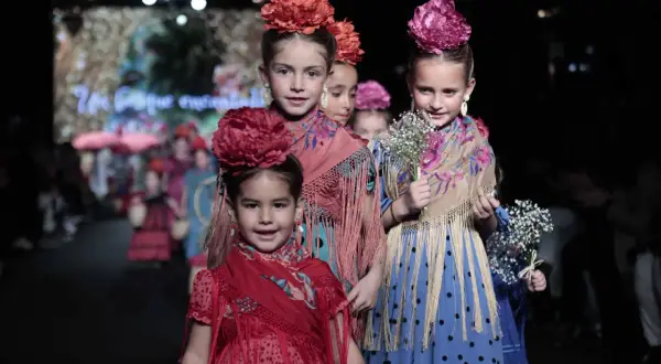 Niñas desfilan con trajes de flamenca, mostrando cómo vestir a un niño de flamenco con flores y mantones.