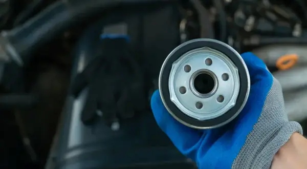 Nowy filtr oleju do silnika 1.6 TDI. Ręka w niebieskiej rękawicy trzyma filtr.
