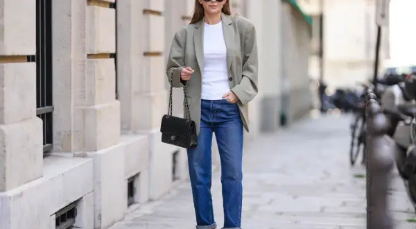 Kobieta w jeansach i oversize'owej marynarce damskiej, z czarną torebką na łańcuszku, prezentuje miejski szyk.