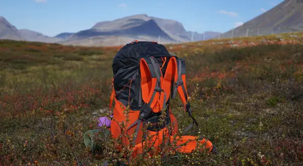 En stor ryggsäck står redo för mat utomhus i fjällterräng. En liggunderlag och en lila kudde syns vid sidan.